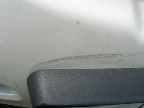 1984 Ford Bronco - Close-up of a white car's body panel showing damage above textured black trim.