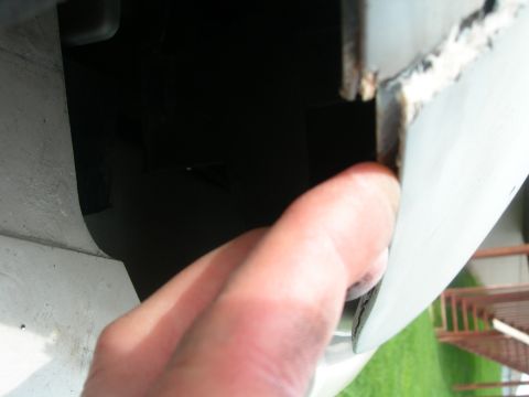 1984 Ford Bronco - A finger inspects the corroded edge of a white vehicle's body panel, showing signs of wear and tear.