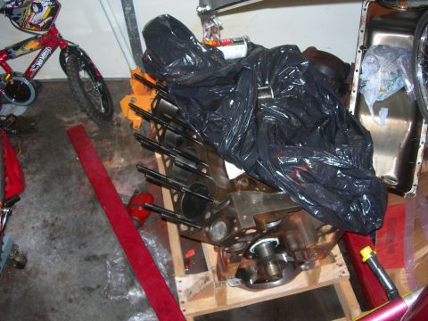 1984 Ford Bronco - An engine block sits on a pallet, partially covered by a black plastic bag, with a bicycle nearby.