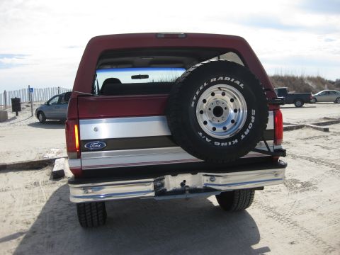 1995 Ford Bronco - Rear view of a red Ford Bronco parked on a sandy area near a beach.