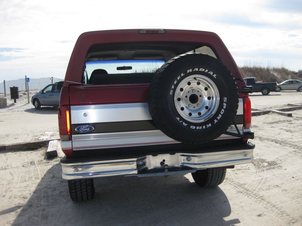Red Ford Bronco with spare tire on rear, chrome bumper, and silver stripe