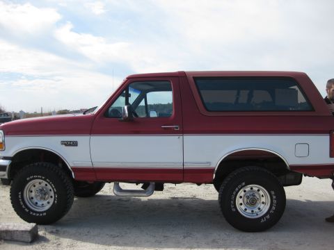 1995 Ford Bronco - Side profile of a two-tone red and white 1995 Ford Bronco SUV parked outdoors.
