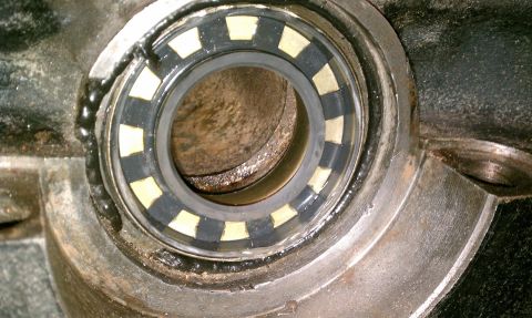 1990 Ford Bronco - Extreme close-up looking down the bore of a cast axle or differential housing, showing a caged brass-colored roller bearing seated in the m…