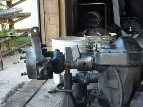 1992 Ford Bronco - Solid front axle assembly removed from a truck and propped on a jack stand outside a shed, viewed end-on down the axle tube toward the cast…