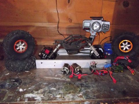 1989 Ford Bronco - RC car parts including motors, shocks, tires, and a remote control transmitter are assembled on a workbench.