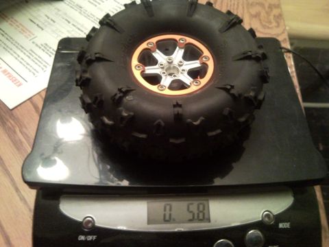 1989 Ford Bronco - A remote-controlled car tire with an orange rim is weighed on a digital scale.