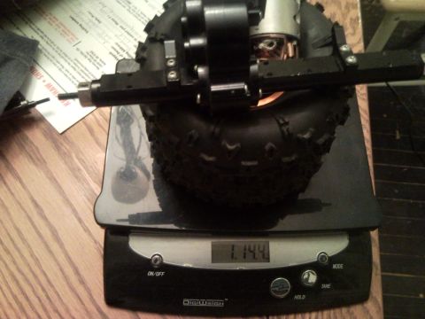 1989 Ford Bronco - A component of an RC car, likely a suspension assembly and tire, is placed on a digital scale.