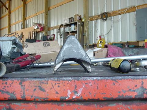 1992 Ford Bronco - A metal bracket sits on a workbench in a garage, surrounded by tools and supplies.