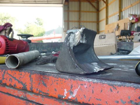 1992 Ford Bronco - A close-up view of a damaged metal component resting on a workbench, surrounded by various tools and equipment.