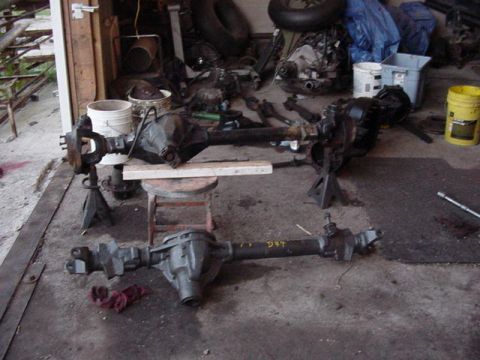 1992 Ford Bronco - Several vehicle axles are laid out on the floor and on jack stands inside a cluttered garage.
