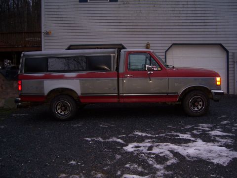 1989 Ford F-150 - This pickup truck, likely from the late 1980s, is parked in a driveway with a camper shell on the bed.