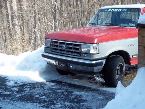 1989 Ford F-150 - This two-tone red and white 1989 Ford F-150 is partially obscured by snowdrifts.