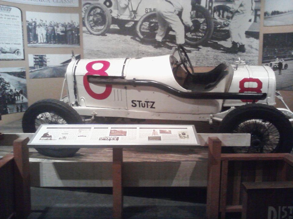 White Stutz race car with red number 8, black interior, wire wheels, and a display board in front