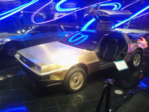 1995 Ford Taurus - A DeLorean DMC-12 is displayed indoors with its distinctive gullwing doors open, illuminated by blue neon lights.