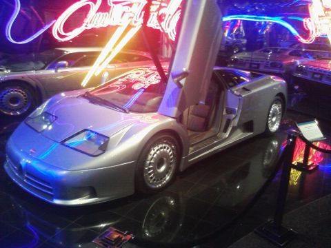 1995 Ford Taurus - A silver sports car with its distinctive butterfly doors open is displayed indoors, illuminated by neon lights.