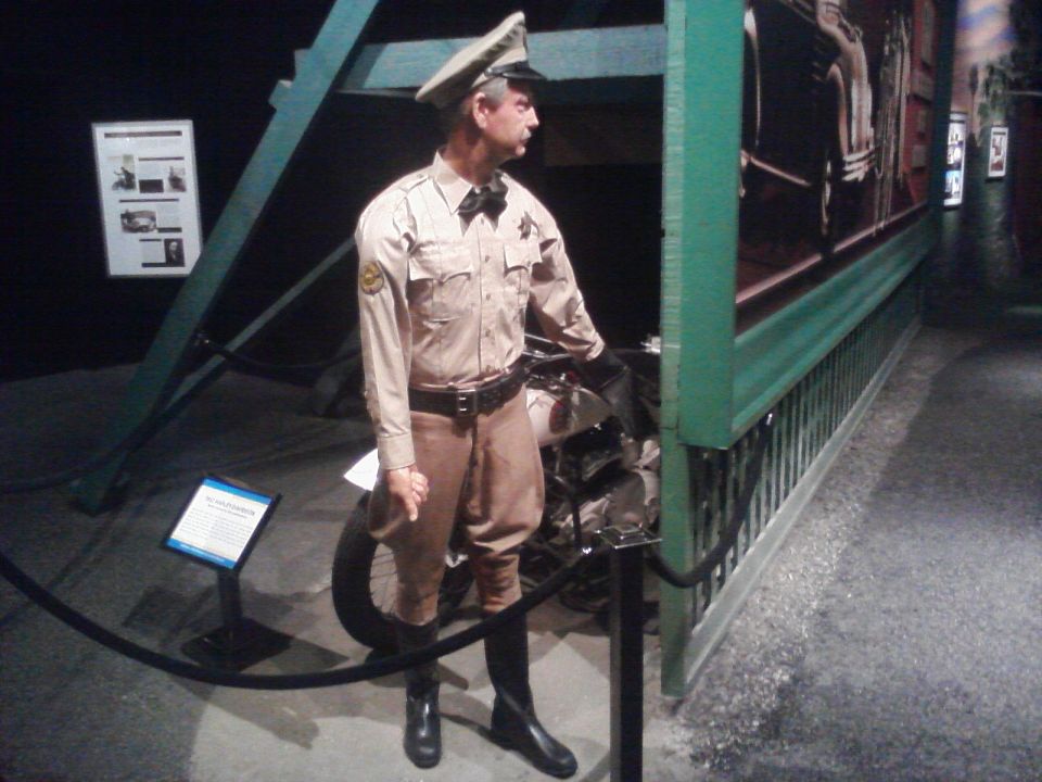 Mannequin dressed as a police officer stands next to a motorcycle in a museum exhibit