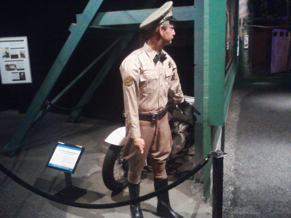 Mannequin dressed as a police officer stands next to a motorcycle in a museum exhibit