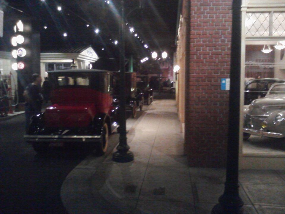 Several vintage cars lined up in a museum exhibit, with a red and black car in the foreground