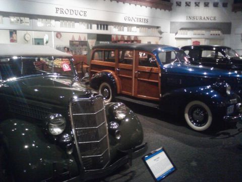 1995 Ford Taurus - A museum exhibit displays vintage cars, including a woody wagon and a dark green car.