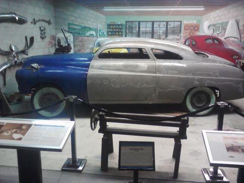 1995 Ford Taurus - A customized coupe, unfinished with blue and primer sections, is displayed alongside a red car in a museum setting.