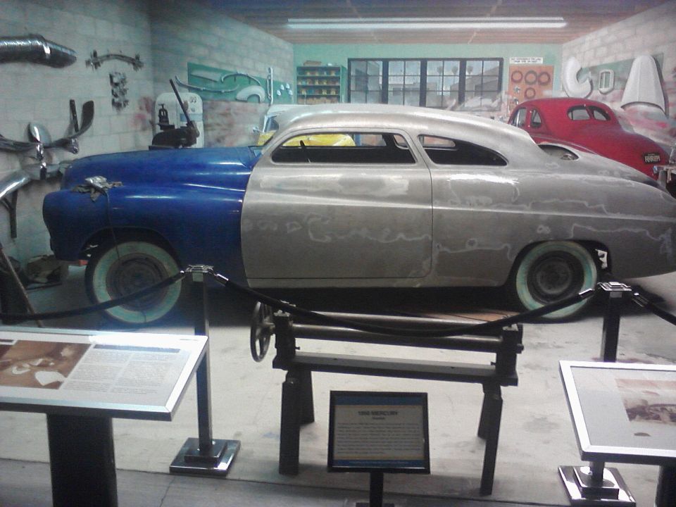 Side view of a customized coupe, half blue and half primer, with a red car in the background
