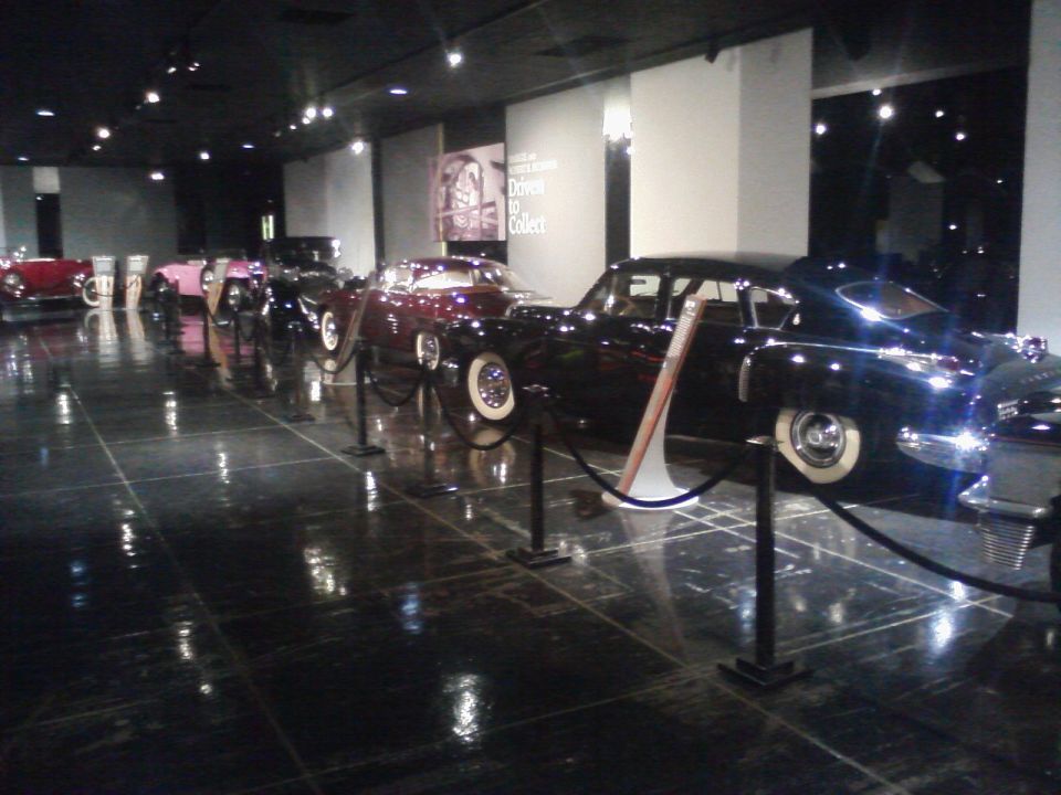Several classic cars lined up in a museum display, with reflective flooring