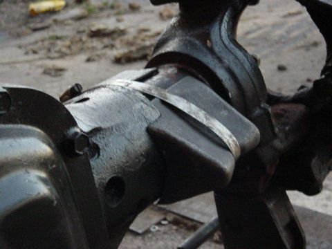 1992 Ford Bronco - Close-up of a cast axle housing with a heavy fabricated steel truss or bracket clamped over the tube by a wide flat strap, sitting on a sho…
