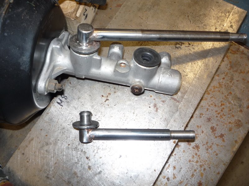 Aluminum brake master cylinder on black booster with two pushrods on a bench