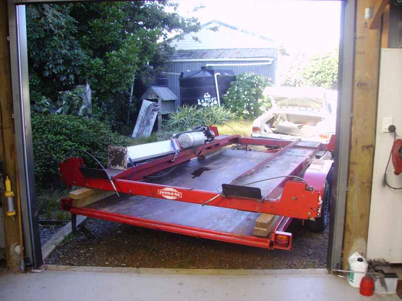 Red tilt-deck single-axle car trailer parked outside an open garage door