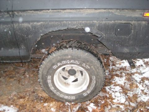 1979 Ford Bronco - A close-up view of a vehicle's side, showing a worn wheel well and tire in a muddy, snowy environment.