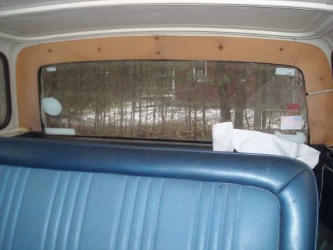 1979 Ford Bronco - Interior view from the rear seat, looking through the back window at a wooded area.