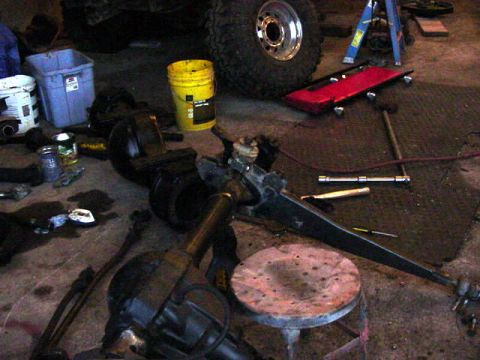 1992 Ford Bronco - Various vehicle axle and suspension components are disassembled and scattered on the ground in a workshop setting that appears to be a gara…