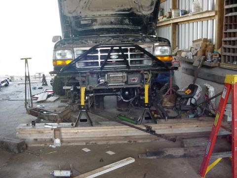 1992 Ford Bronco - Front end of a 1992 Ford Bronco undergoing repairs in a workshop, supported by jack stands.