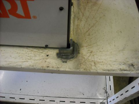 1979 Ford F-150 - Close-up of a welded metal bracket on a shelf, with a partial orange logo visible on a panel above.
