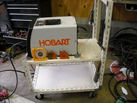 1979 Ford F-150 - A Hobart welding machine sits on a multi-tiered cart, accompanied by a scale and magnetic clamps.
