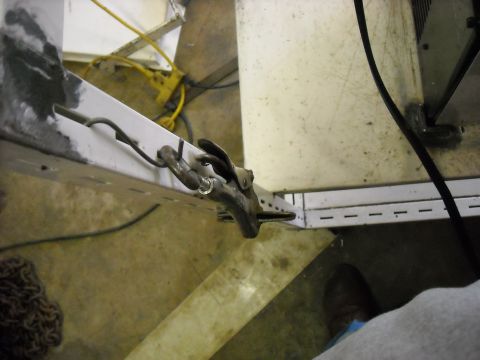 1979 Ford F-150 - A close-up view of a metal clamp fastened to a white structural beam, with a black wire extending from it.