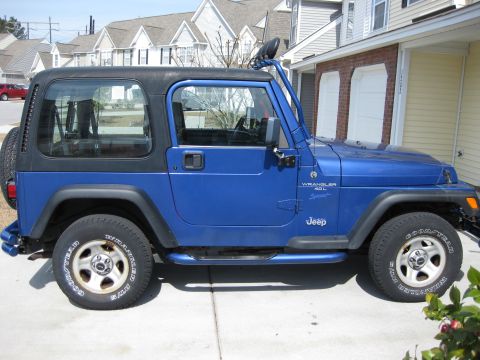 1998 Jeep Wrangler - A blue Jeep Wrangler is parked in front of a residential building. The vehicle has a black hardtop and visible side steps.