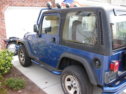 1998 Jeep Wrangler - Blue Jeep Wrangler with aftermarket roll cage and lights parked in front of a garage. Motorcycle is visible.