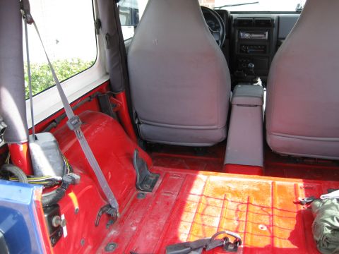 1998 Jeep Wrangler - Interior view of a Jeep showing the red floor, grey seats, and dashboard with a Supermotors logo.
