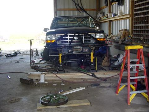 1992 Ford Bronco - A black 1992 Ford Bronco is elevated on jack stands in a garage, undergoing work.
