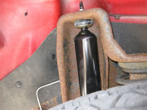 1998 Jeep Wrangler - Close-up of a rusty shock absorber mount on a red vehicle, with a black shock absorber and tire visible.