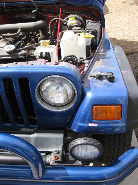 1998 Jeep Wrangler - The engine bay of a blue Jeep Wrangler is visible with the hood open, revealing various mechanical parts.