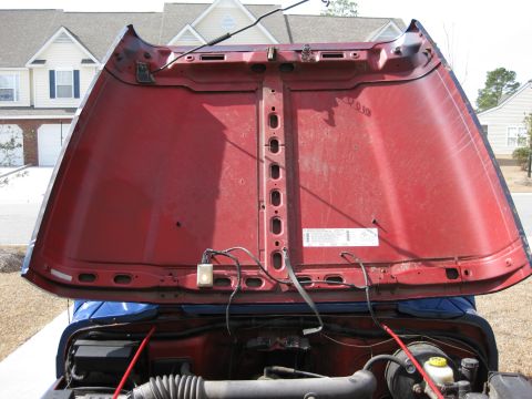 1998 Jeep Wrangler - The underside of a red Jeep Wrangler hood is open, revealing the engine compartment and various wires.