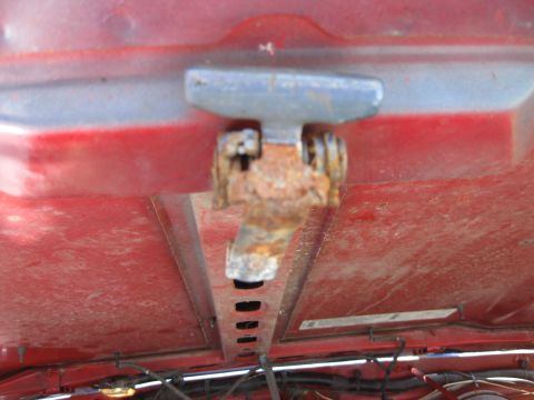1998 Jeep Wrangler - Close-up of a rusty hood hinge on a red vehicle, with a website logo visible at the bottom.