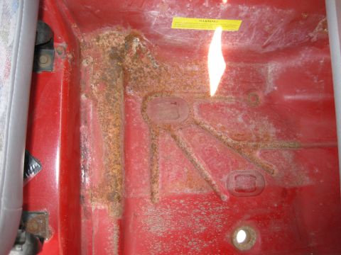 1998 Jeep Wrangler - The interior floor pan shows significant rust damage, with a yellow warning sticker visible on the upper right.