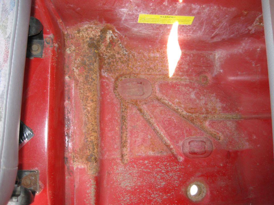 Rusted red interior floor pan with yellow warning sticker