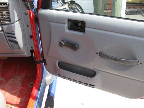 1998 Jeep Wrangler - Interior door panel of a Jeep Wrangler, showing the manual window crank and gray trim.