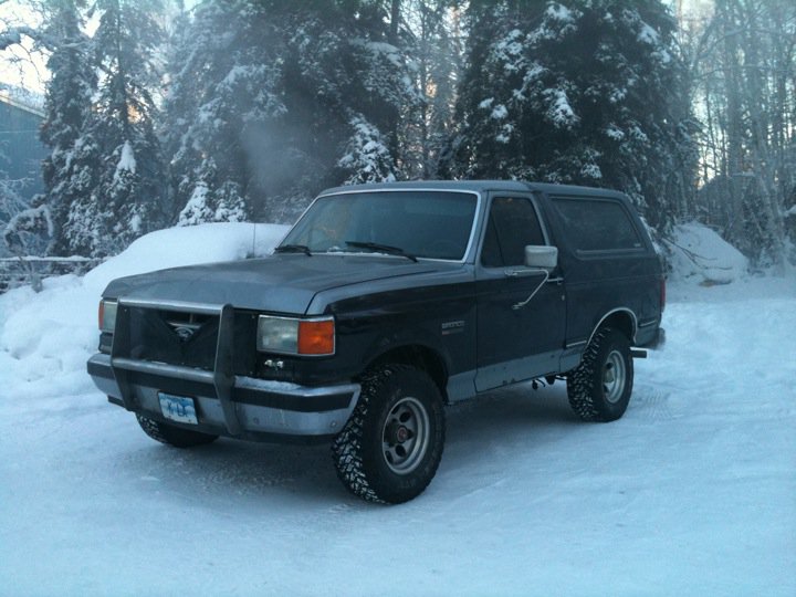 Dark blue and grey Ford Bronco in snow, front bull bar, snow-covered trees in background