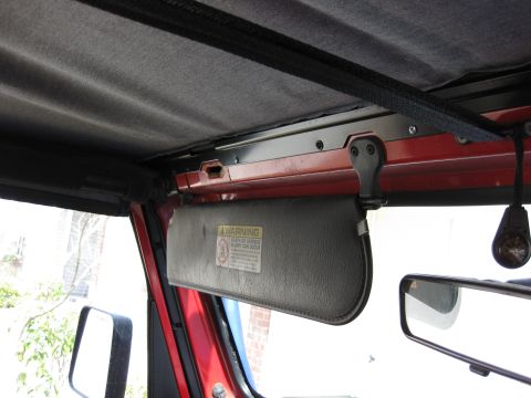1998 Jeep Wrangler - The interior of a red Jeep Wrangler is visible, a sun visor with a warning label and a side mirror.