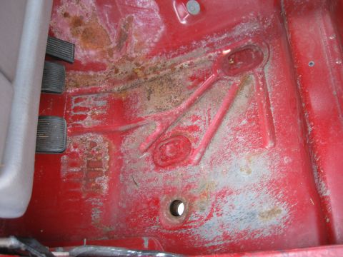 1998 Jeep Wrangler - The red floor pan of a vehicle shows signs of rust and wear around the pedals.
